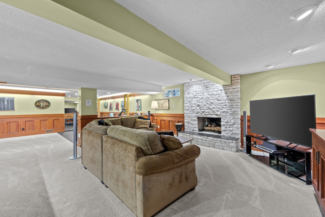 Furnished basement recreation room with a brown sectional, stone fireplace, and television.