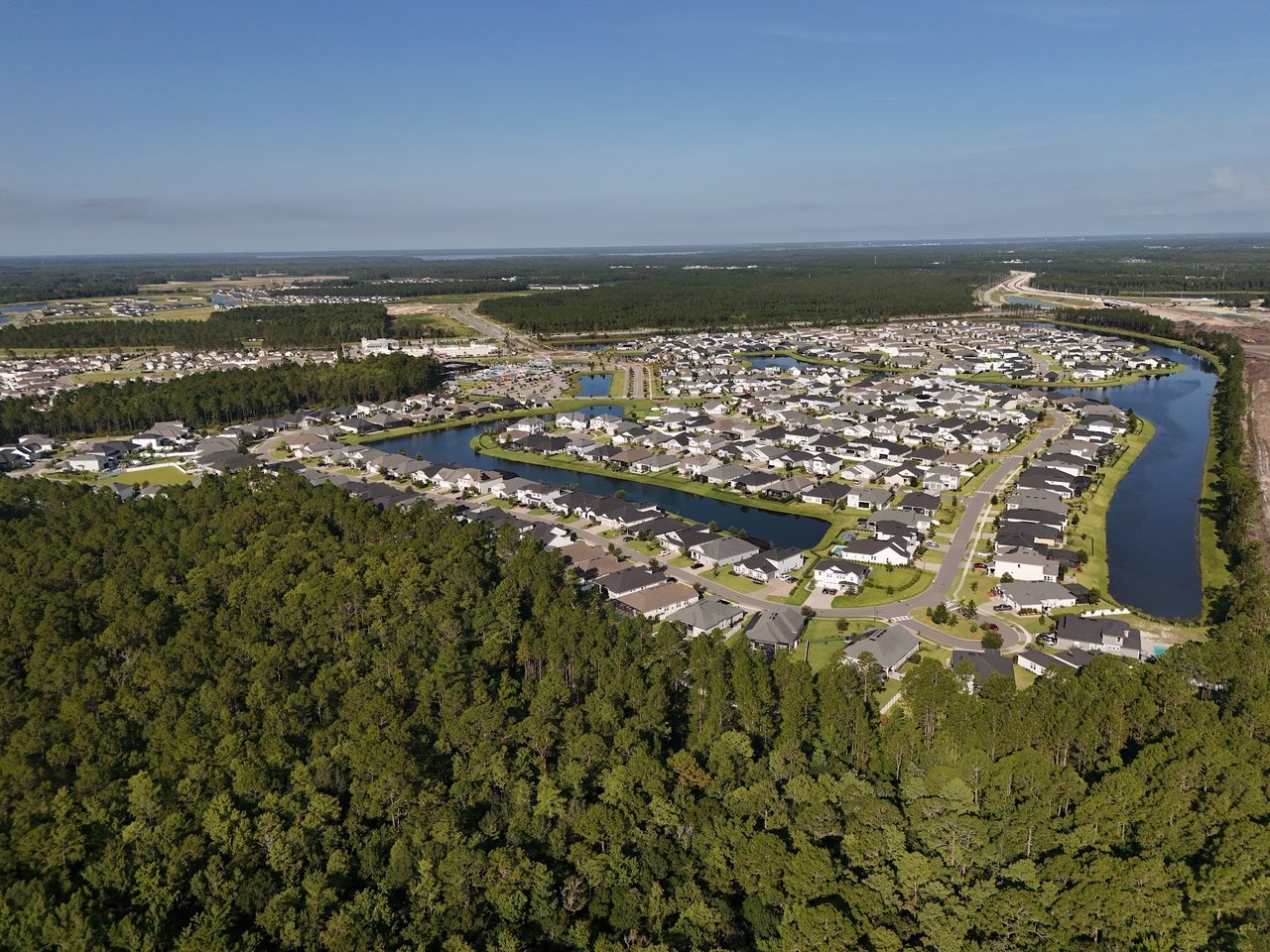 Aerial view of a residential neighborhood with homes beside winding ponds and surrounding woodland.