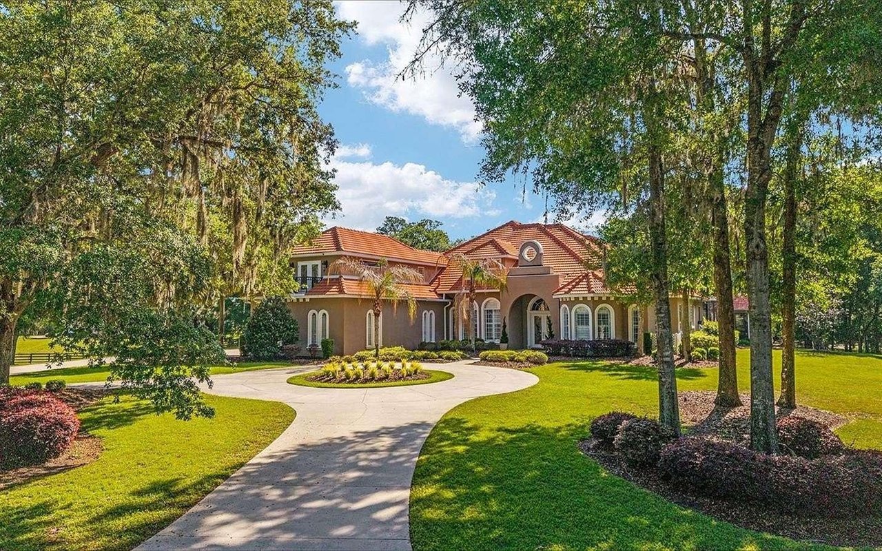 Mediterranean-style home with a red tile roof, arched entrance, and curved circular driveway.