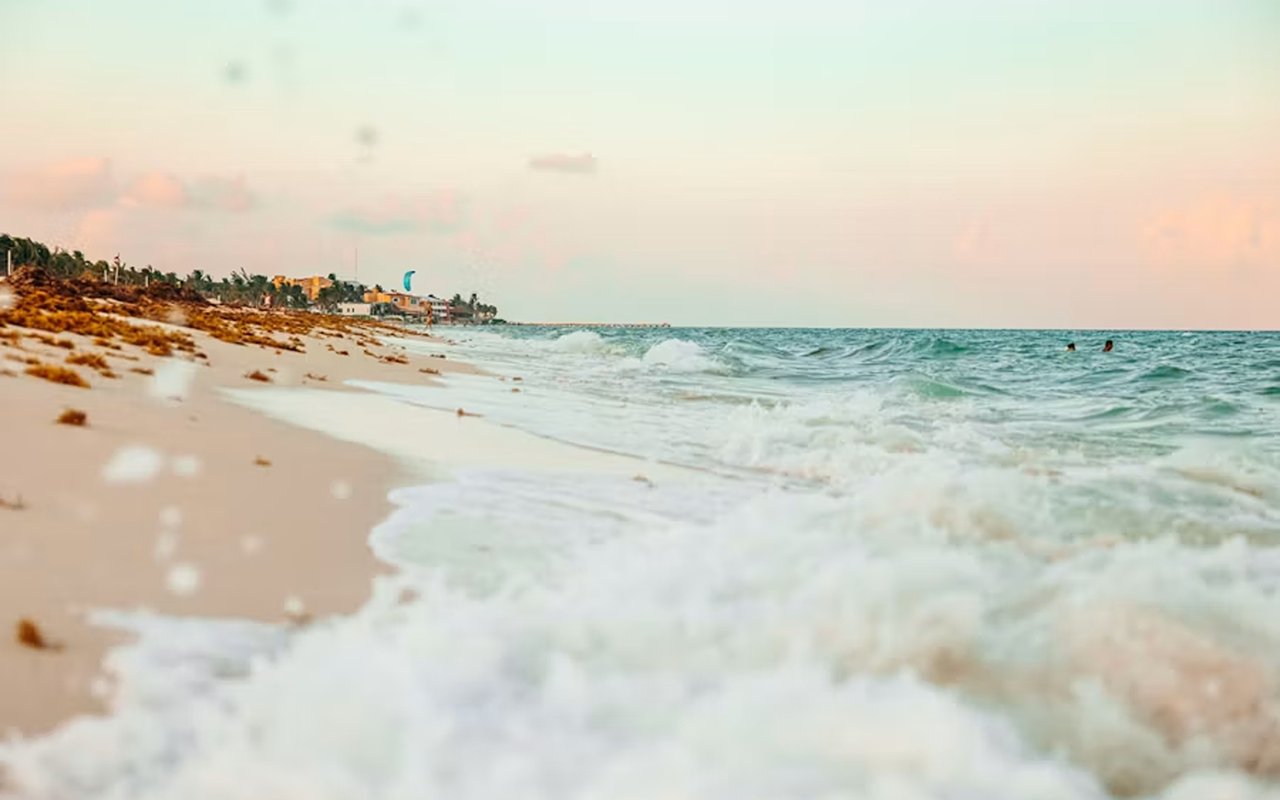 Gulf Coast beach at golden hour, with foamy waves, coastal homes in the distance, and two swimmers.