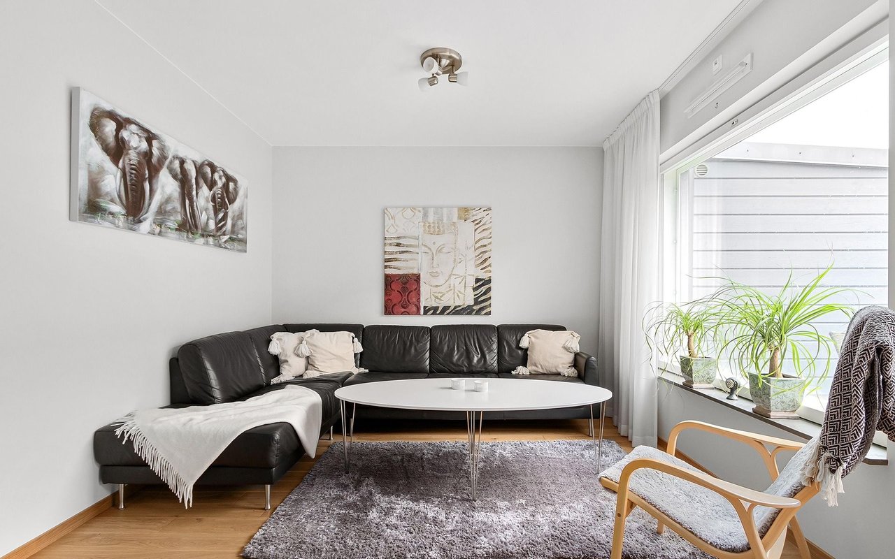 Living room with a leather sectional, oval coffee table, and plants by a large window.