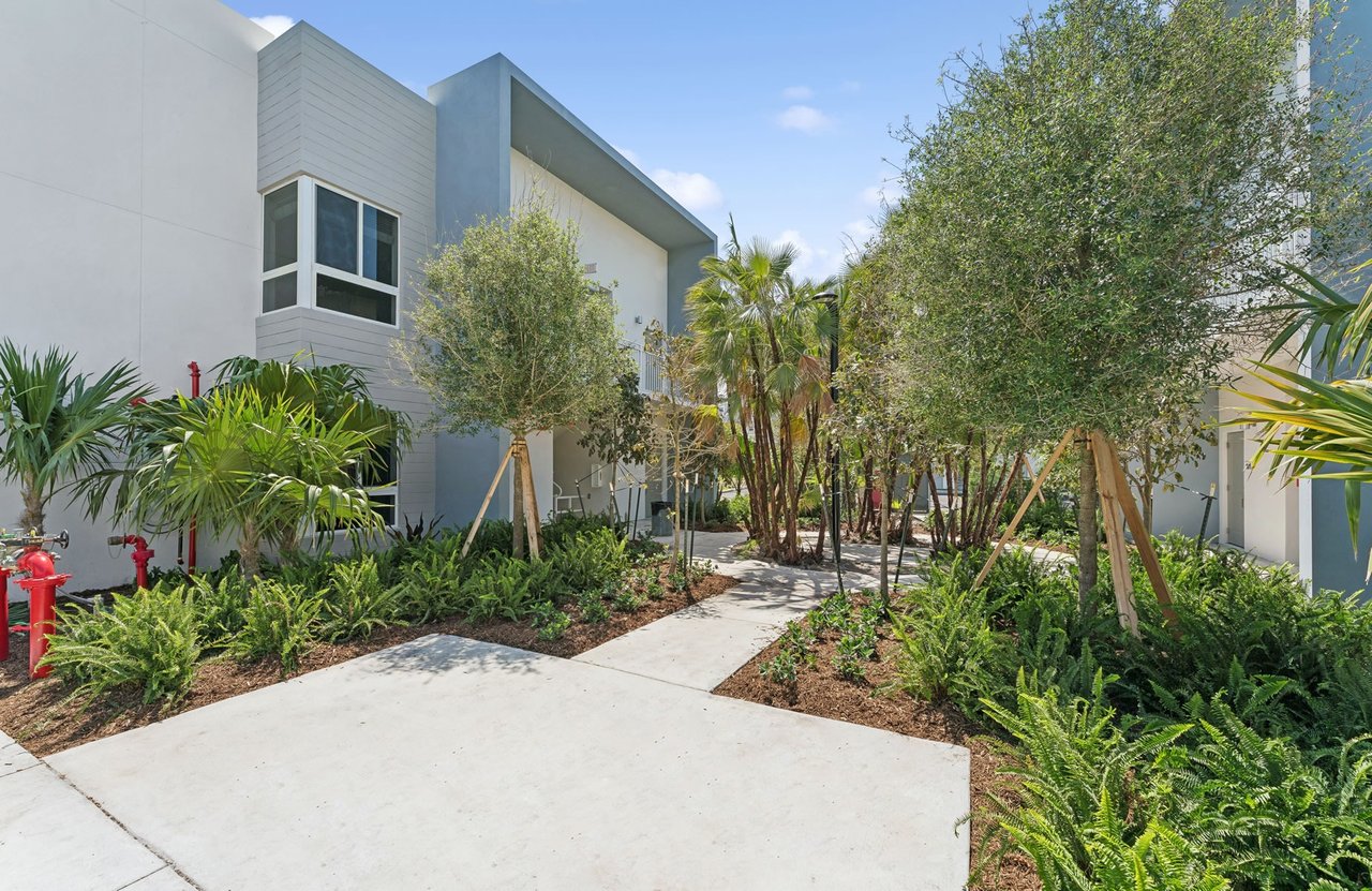 Modern residential building beside a landscaped courtyard with a curving walkway and palm trees.