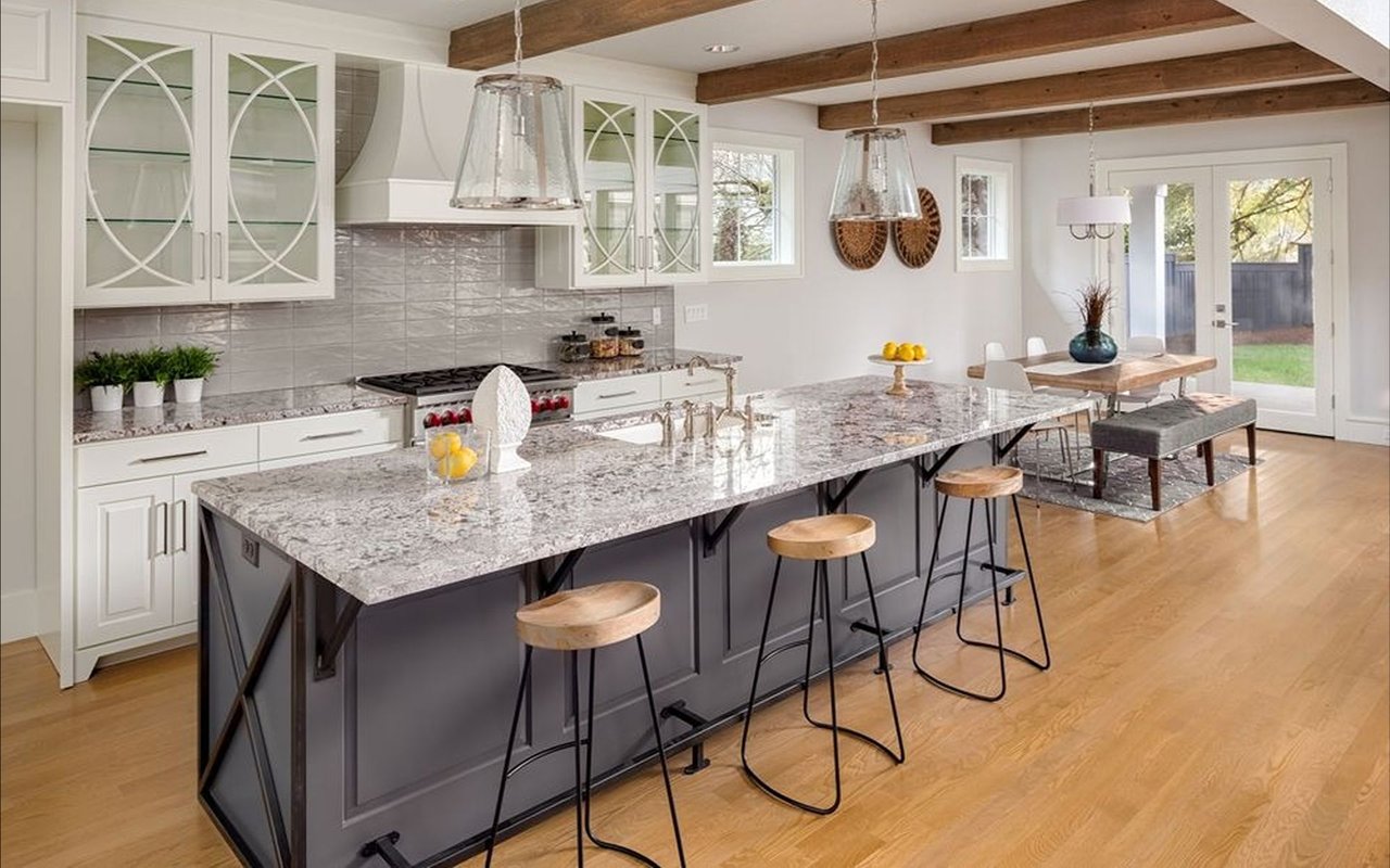 Renovated kitchen with a large granite island, glass-front cabinets, and exposed wood ceiling beams.