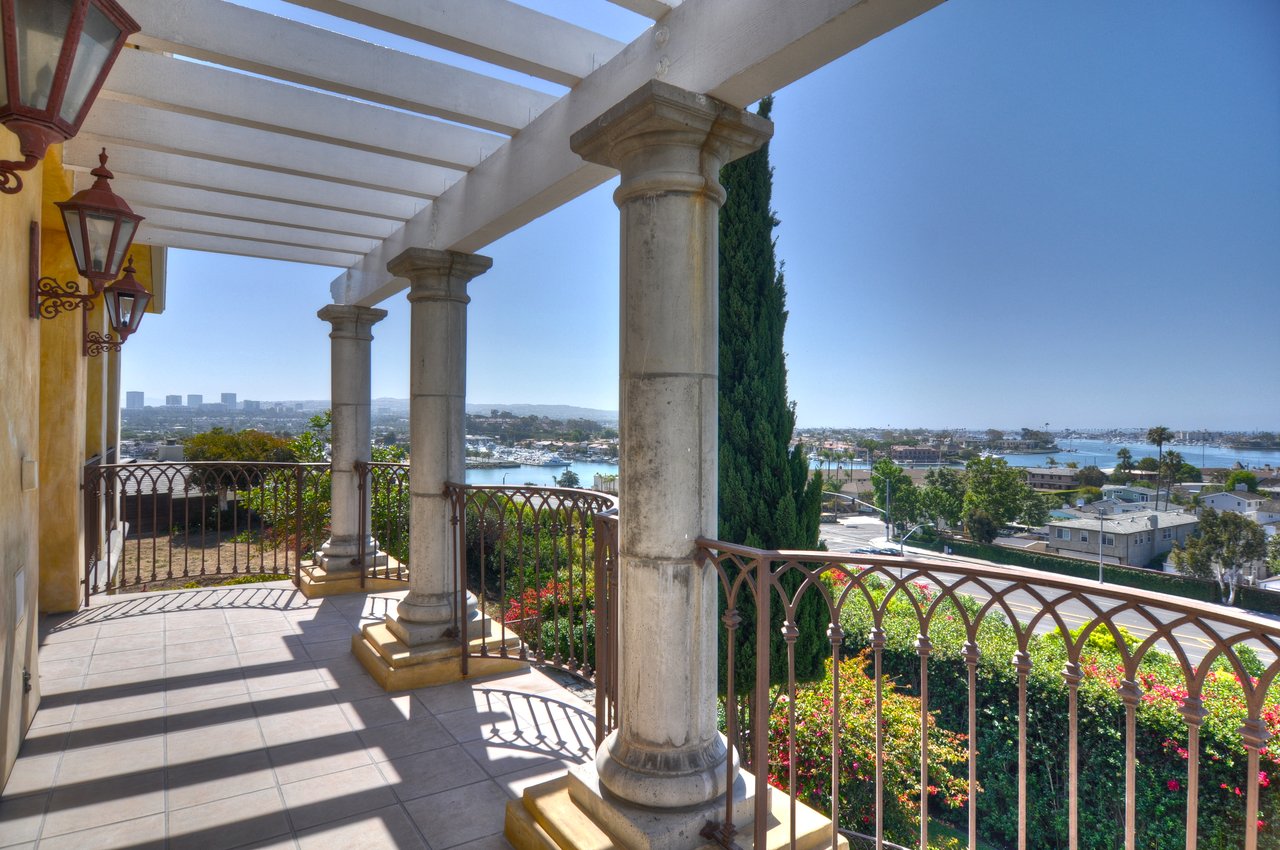 Harbor-view terrace with a white pergola, stone columns, and decorative iron railings.