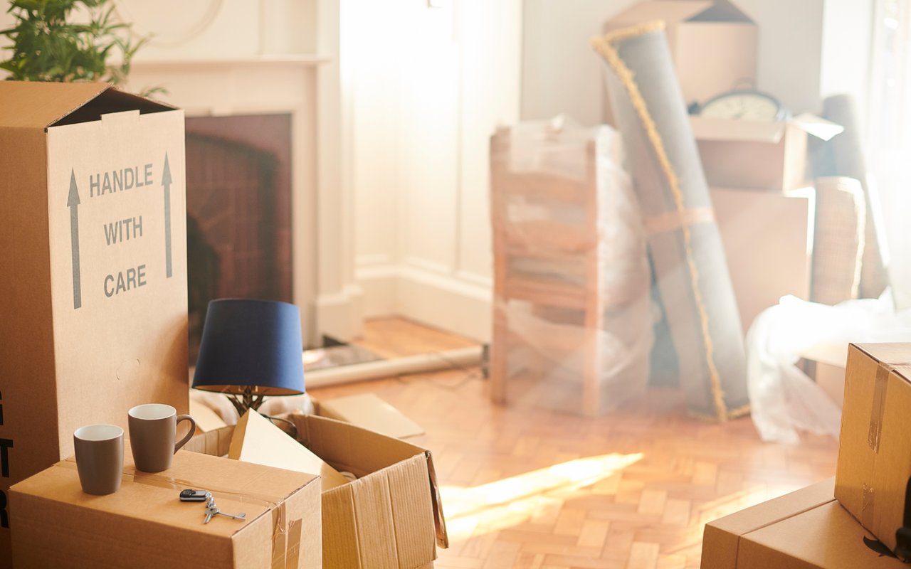 Moving boxes in a sunlit room, with a handle-with-care label and household items packed nearby.