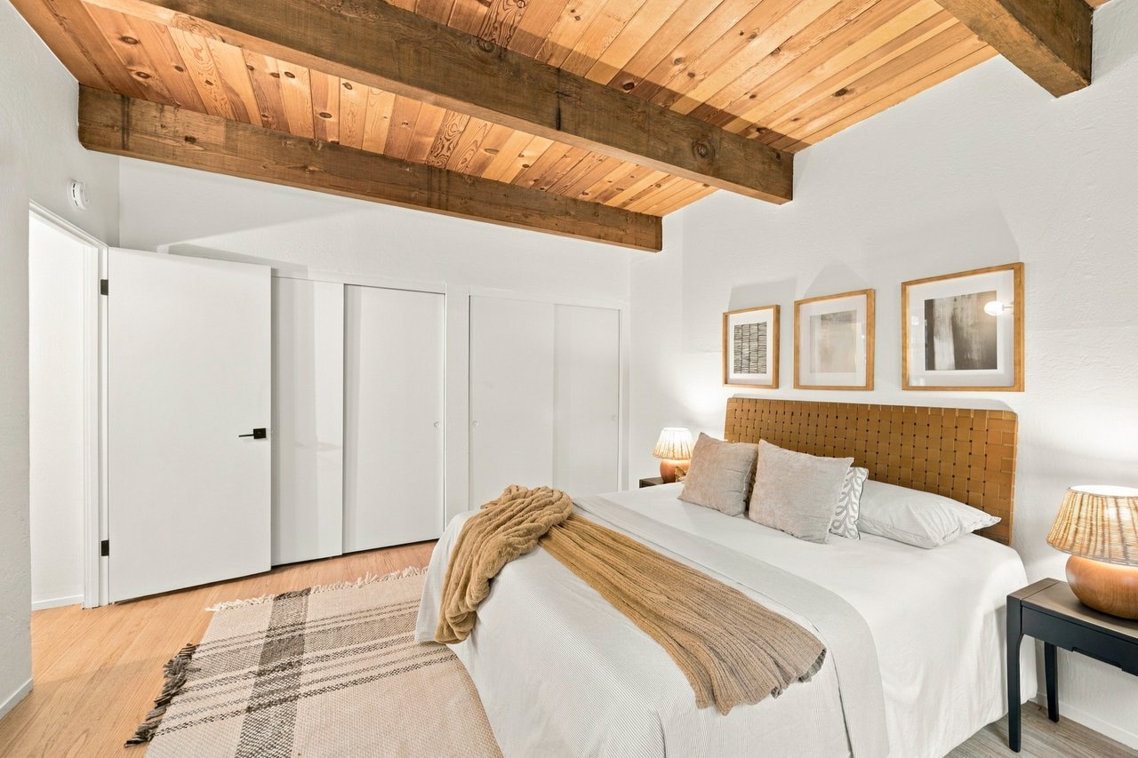 Bedroom with a white bed beneath a warm wood-plank ceiling and exposed beams.