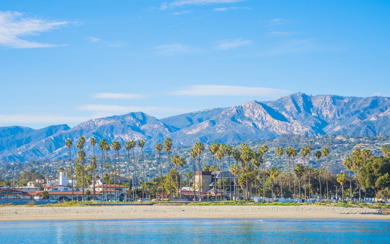 Palm-lined beach and coastal city beneath rugged mountains.