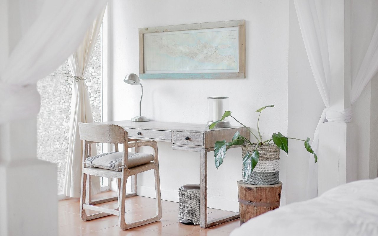 Bright bedroom desk nook with a wooden desk, framed map, and leafy potted plant.