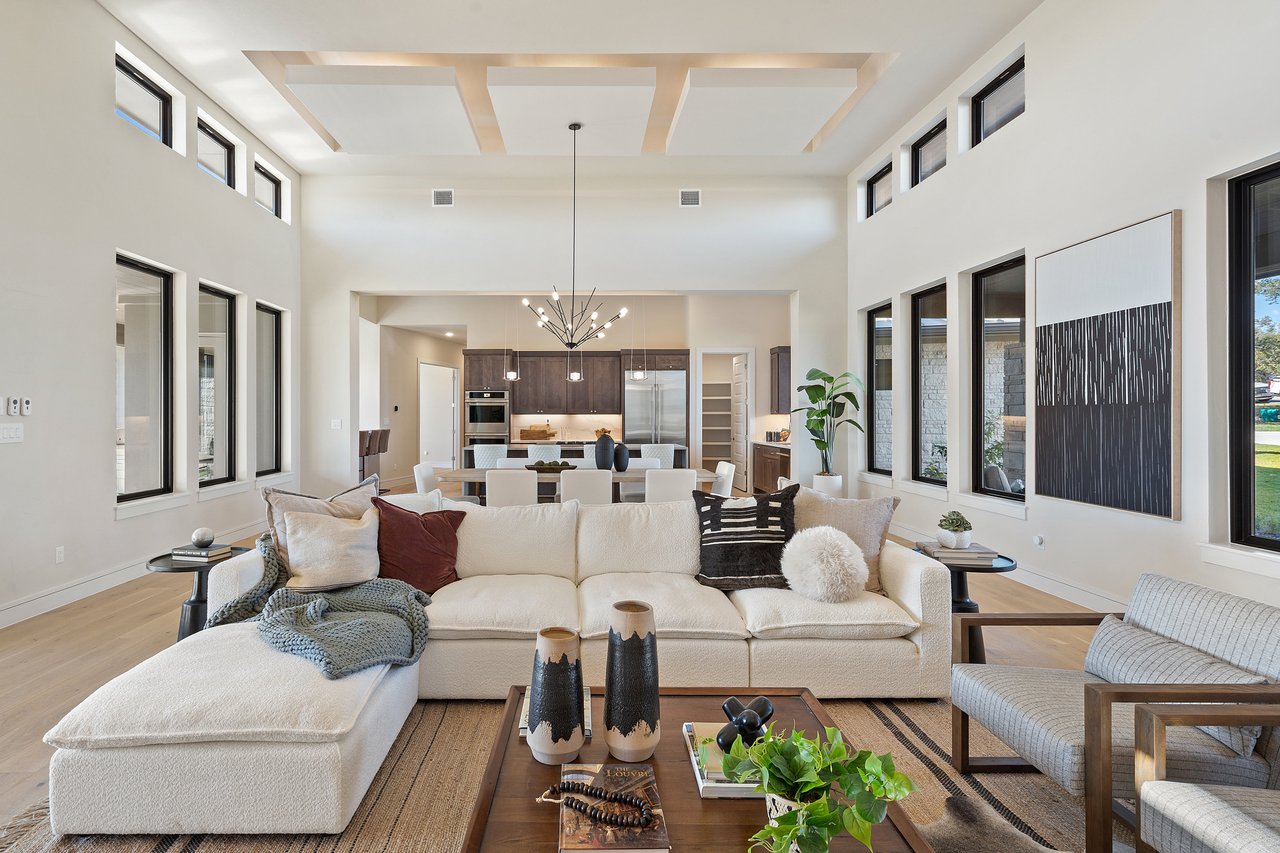 Living room with a coffered ceiling, sectional sofa, and chandelier, open to the kitchen, at this Bee Caves home on Caudill Lane, Austin, Texas.