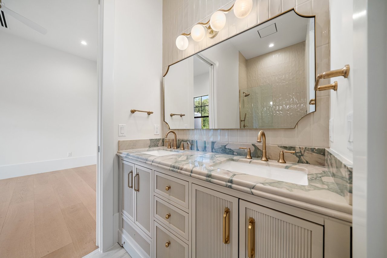Bathroom with a double vanity, marble counters, brass fixtures, and a large mirror.