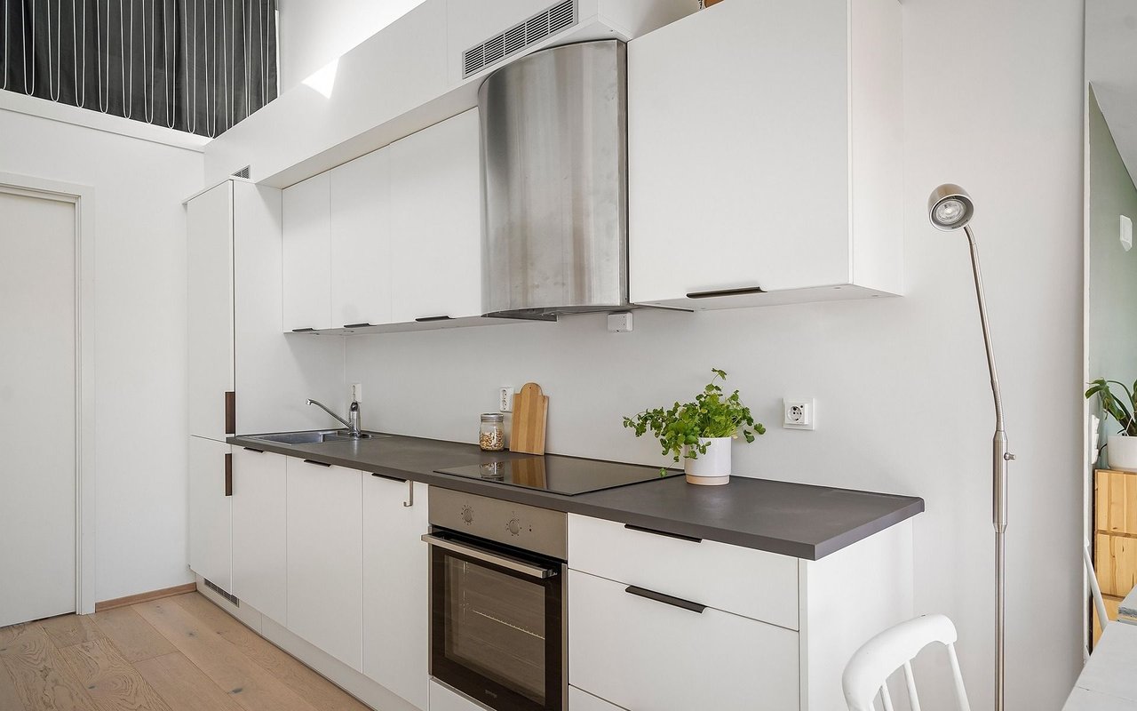 Modern white kitchen with dark countertops, a stainless steel range hood, and wood flooring.