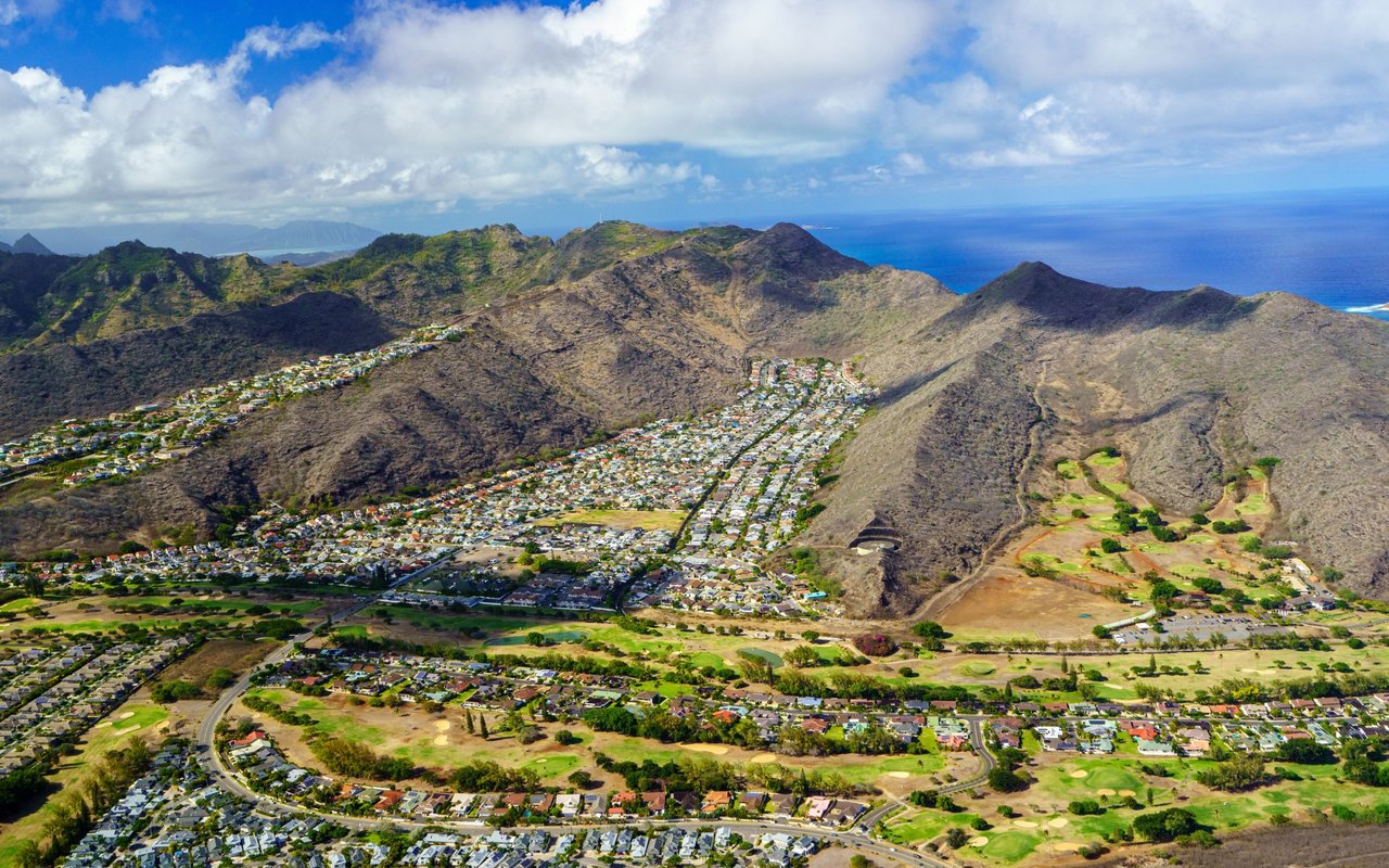Aerial view of homes between rugged ridges, with a golf course and the Pacific Ocean beyond.