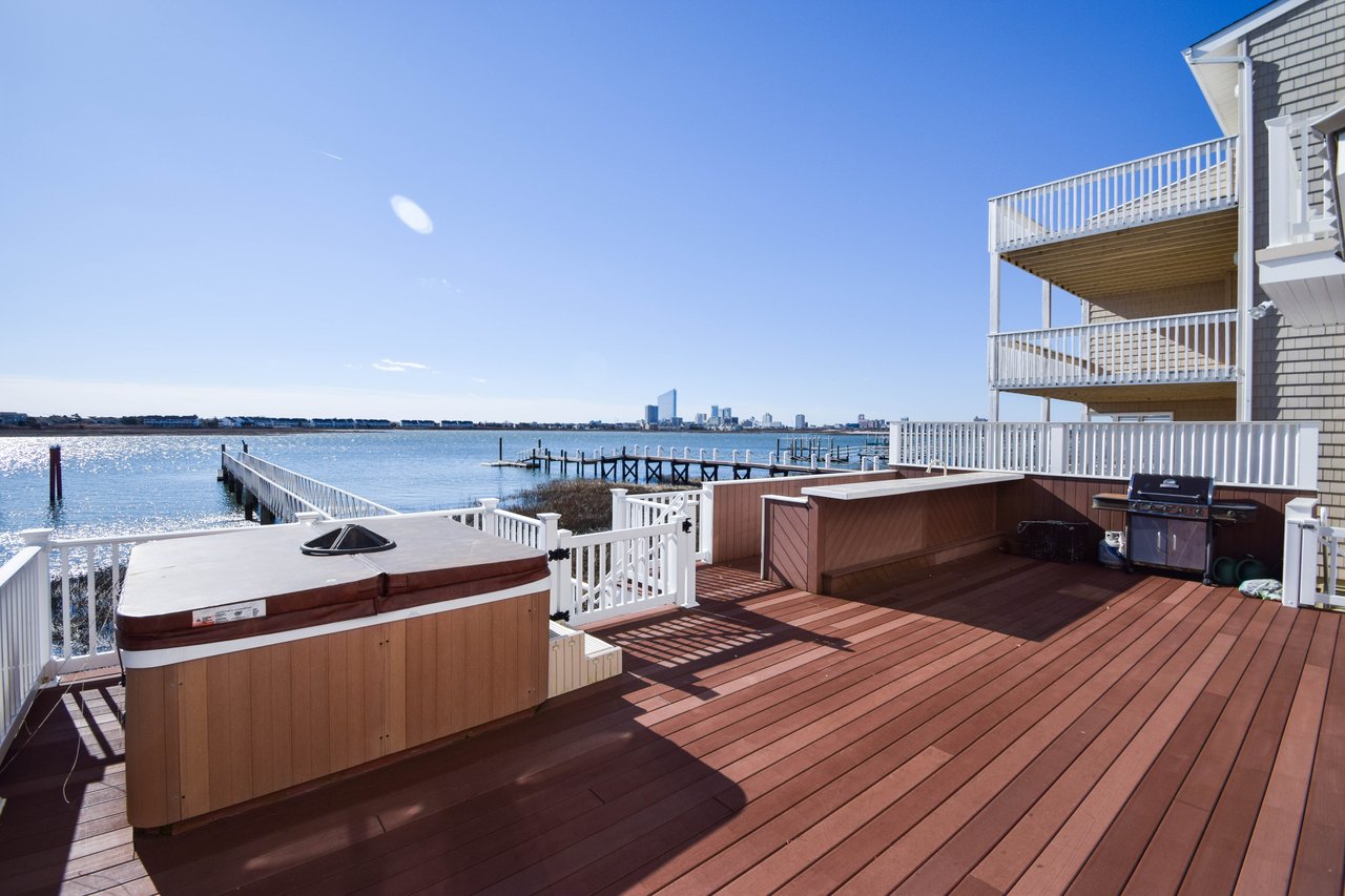 Waterfront deck with a hot tub and grill overlooking a bay and distant skyline.