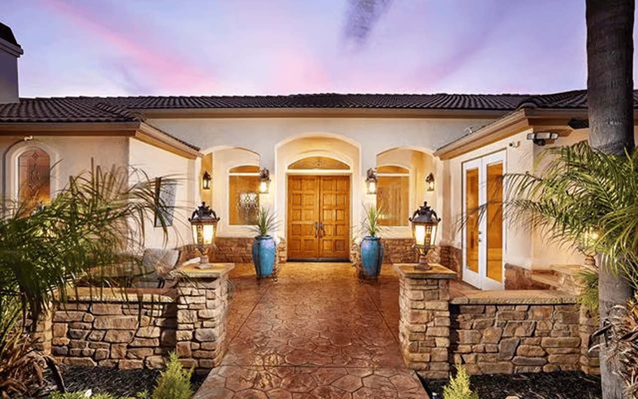 Home entrance with arched windows, double wooden doors, stone planters, and a stamped-stone walkway.