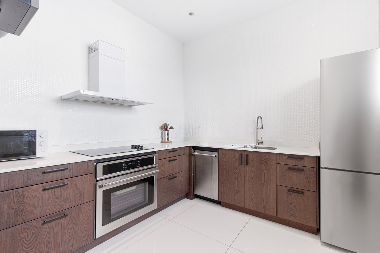 Modern rental kitchen with dark wood cabinets, white counters, and stainless steel appliances.