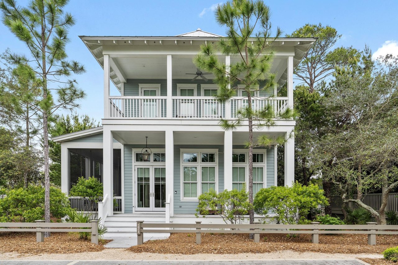 Two-story blue home with a broad covered balcony and screened side porch.