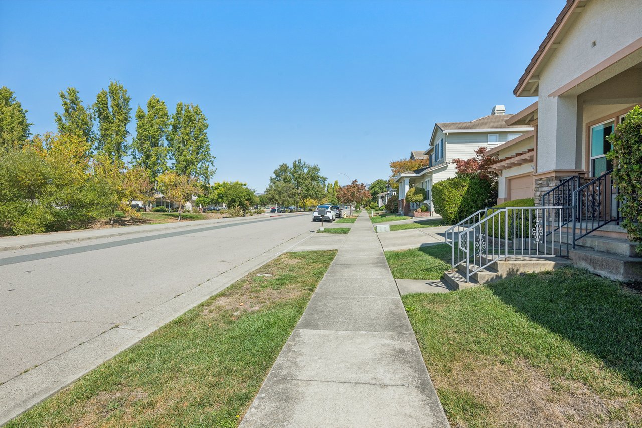 Residential street with a sidewalk and the featured home’s front porch and railings.