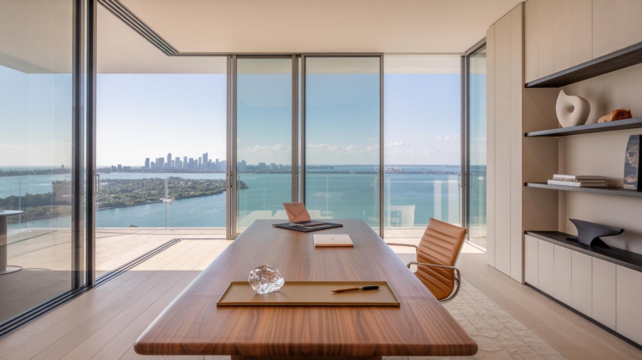 Modern office with a long wooden desk facing floor-to-ceiling windows overlooking a bay and distant skyline.