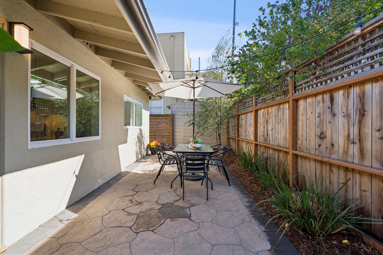 Outdoor patio with a stone-paved floor, dining set, umbrella, and wooden privacy fence.