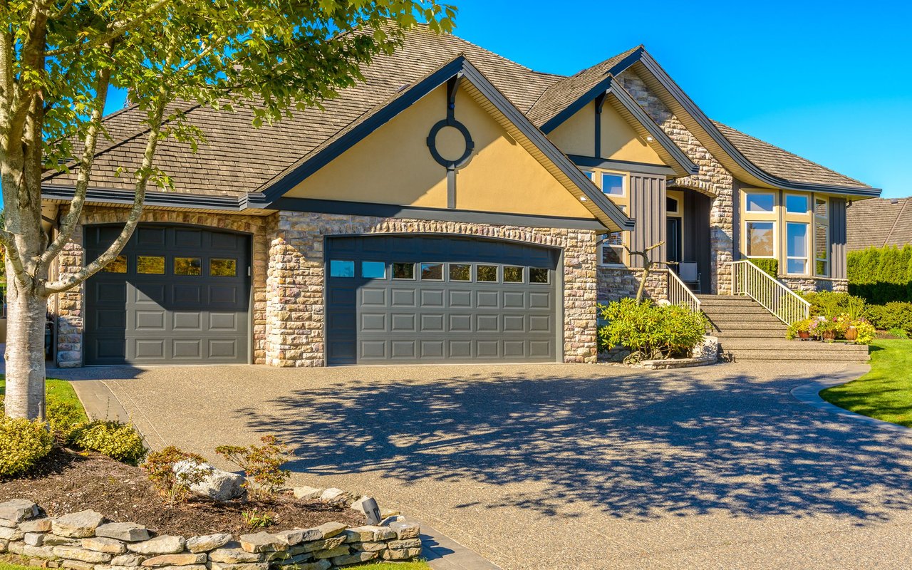 Large stone-and-tan house with two garage doors, a broad driveway, and landscaped front yard.