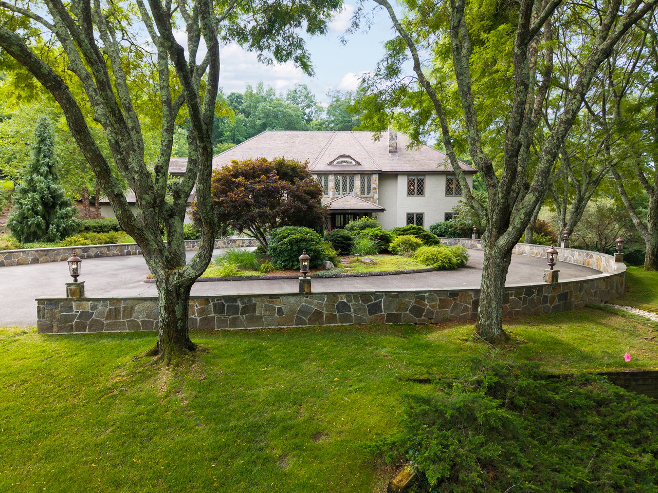 Elevated view of 21 Breezy Knoll, a French château-inspired luxury estate in Avon, Connecticut, with a circular driveway, stone walls, mature trees, and manicured landscaping.