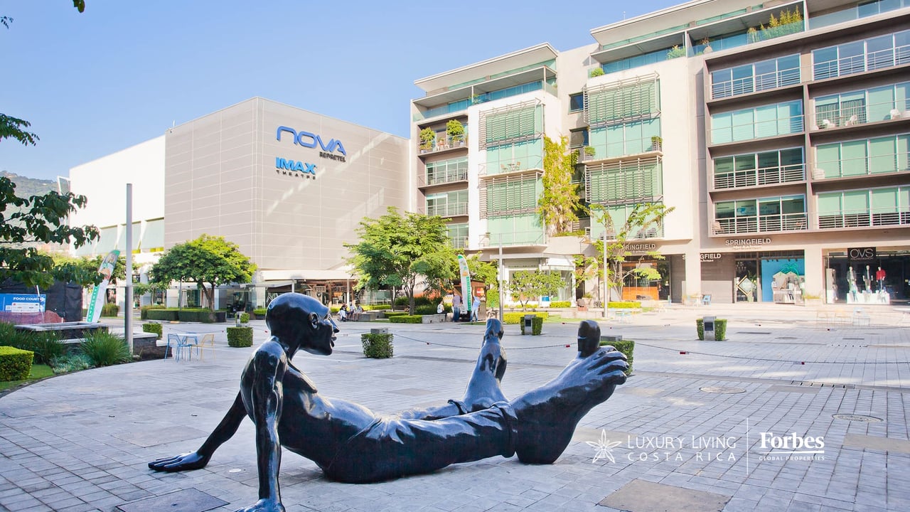 Avenida Escazú plaza buildings and paved courtyard with a reclining black sculpture.