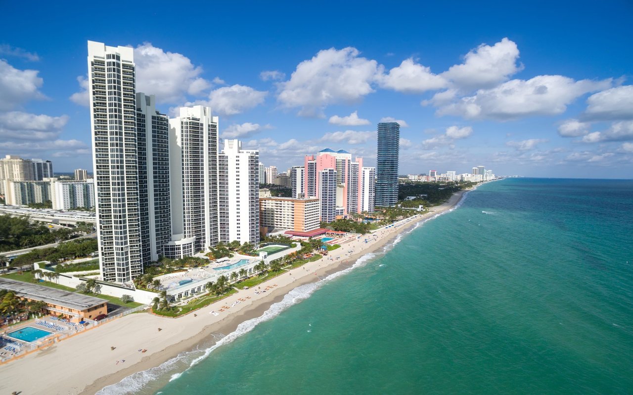 Beachfront high-rise buildings beside a long sandy shore and turquoise water.