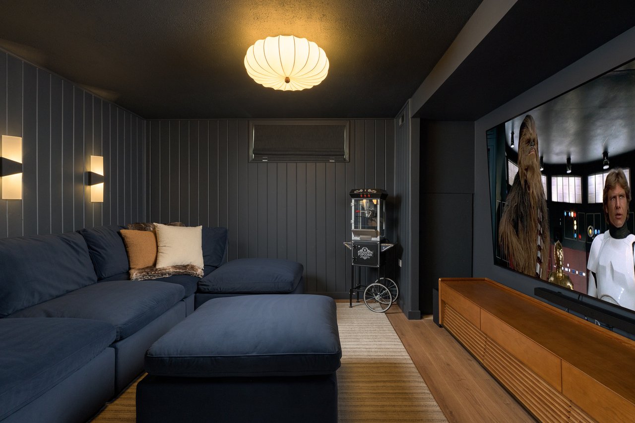 Media room with a navy sectional, dark paneled walls, and a popcorn machine.