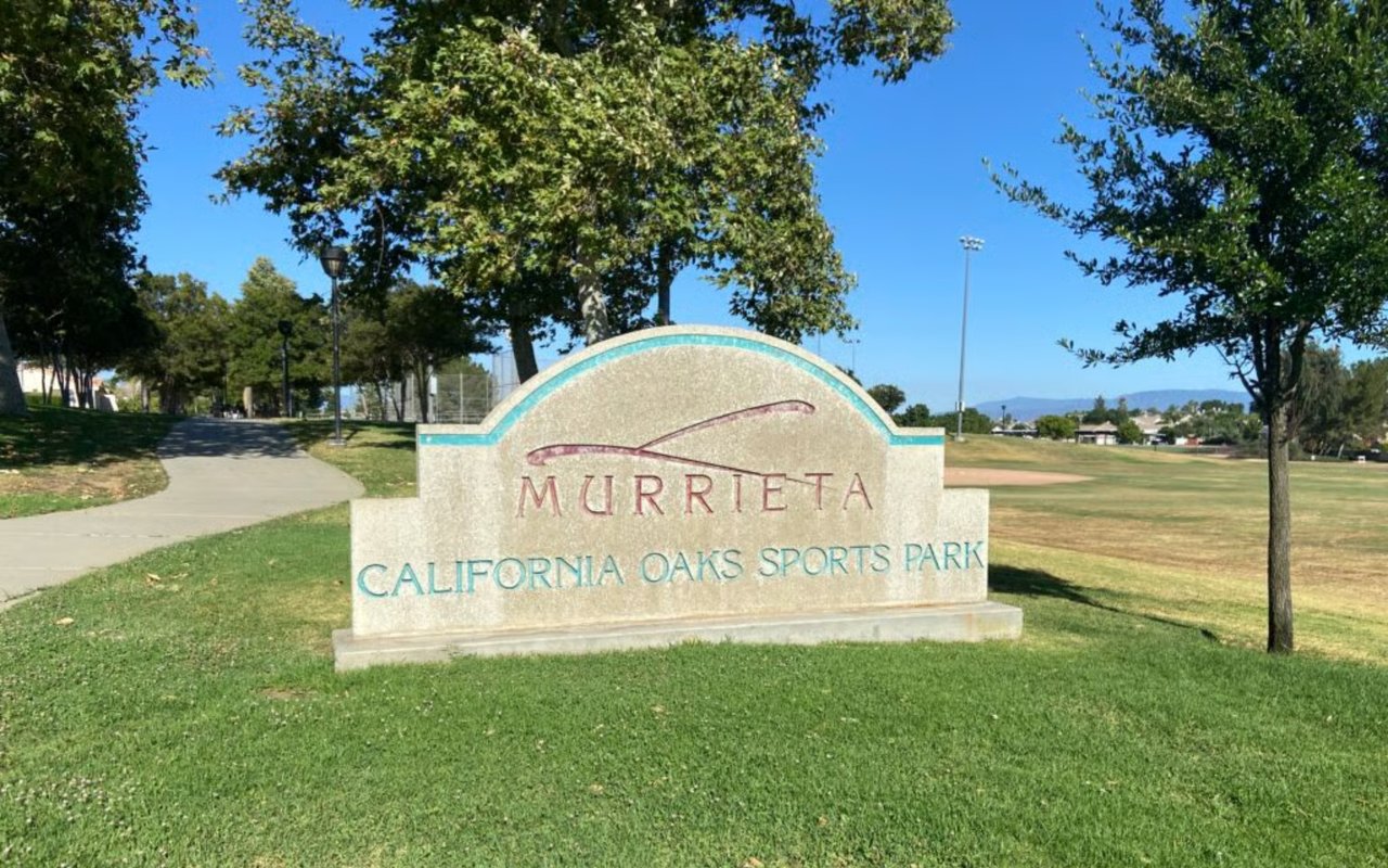 California Oaks Sports Park sign in Murrieta, beside lawns, trees, and a paved walking path.