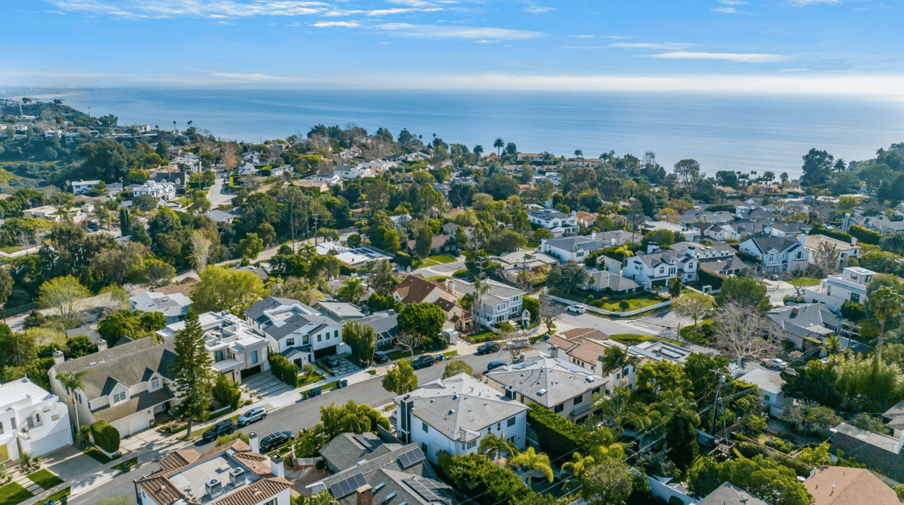 Coastal neighborhood aerial with homes, tree-lined streets, and ocean views.
