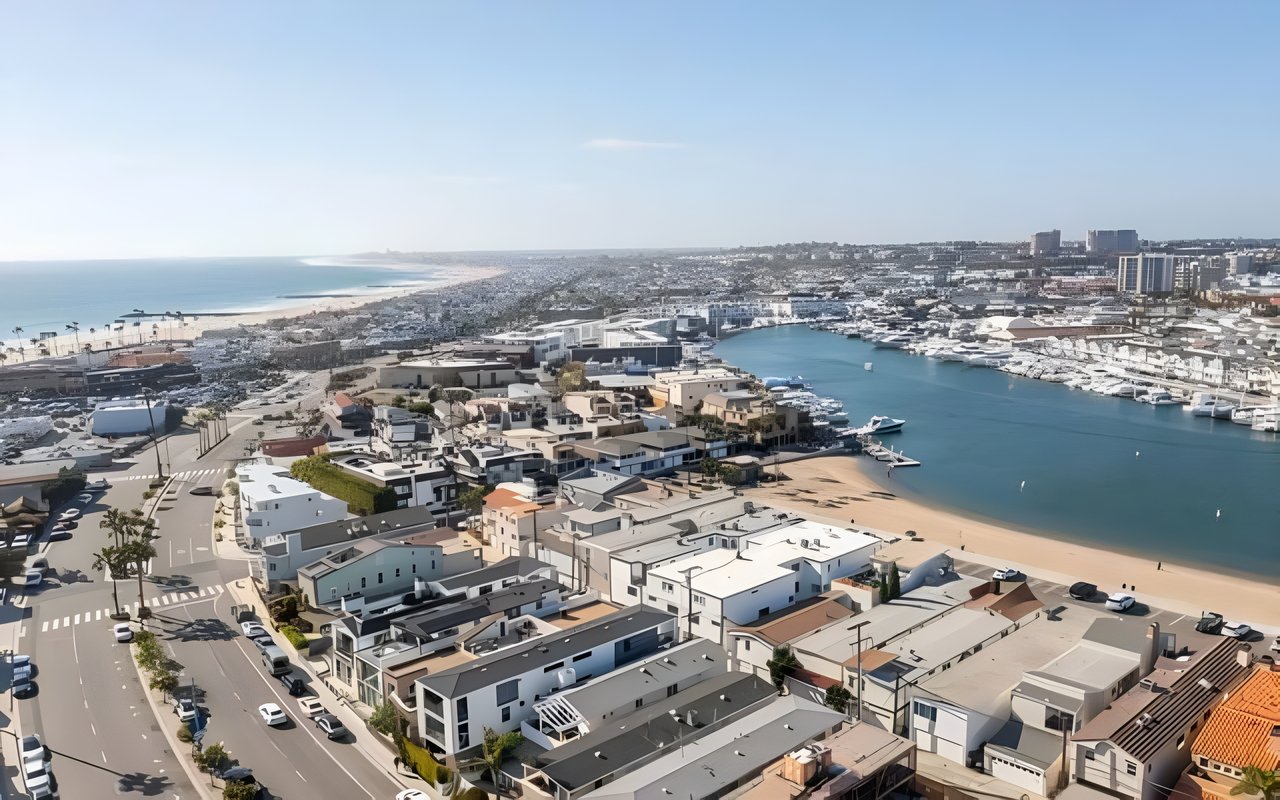  An aerial view of a coastal city with a marina full of boats, a beach, and a residential neighborhood along the water.