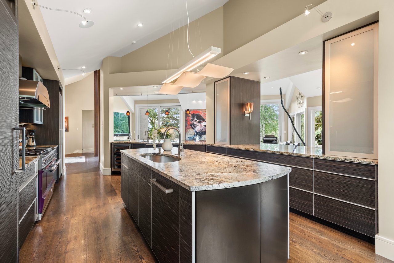 Modern kitchen with a large stone island, dark cabinetry, and sculptural pendant lights.