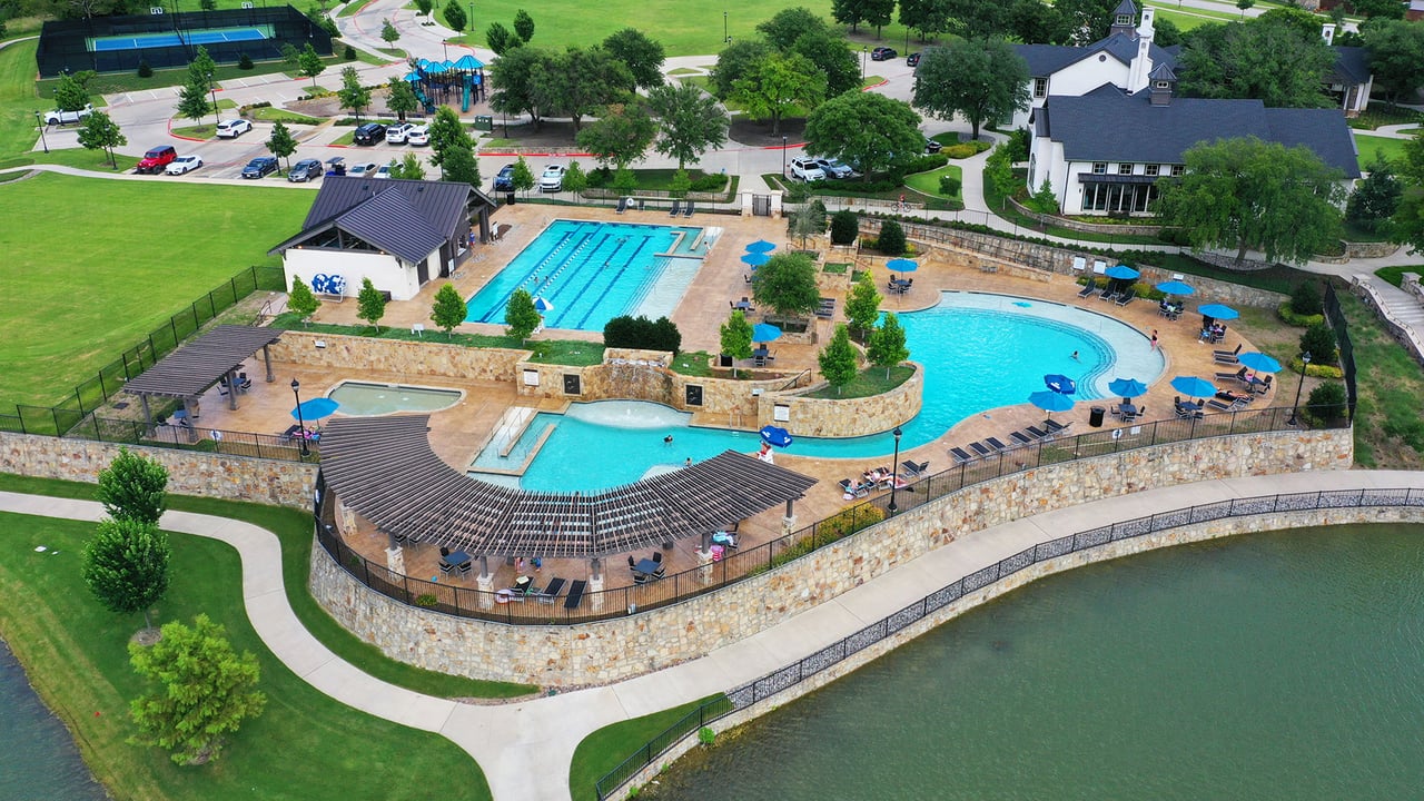 Aerial view of Mustang Lakes resort-style pool complex in Celina TX featuring a lap pool, lagoon pool, pergola seating, tennis courts, and lakeside walking trails in North DFW.