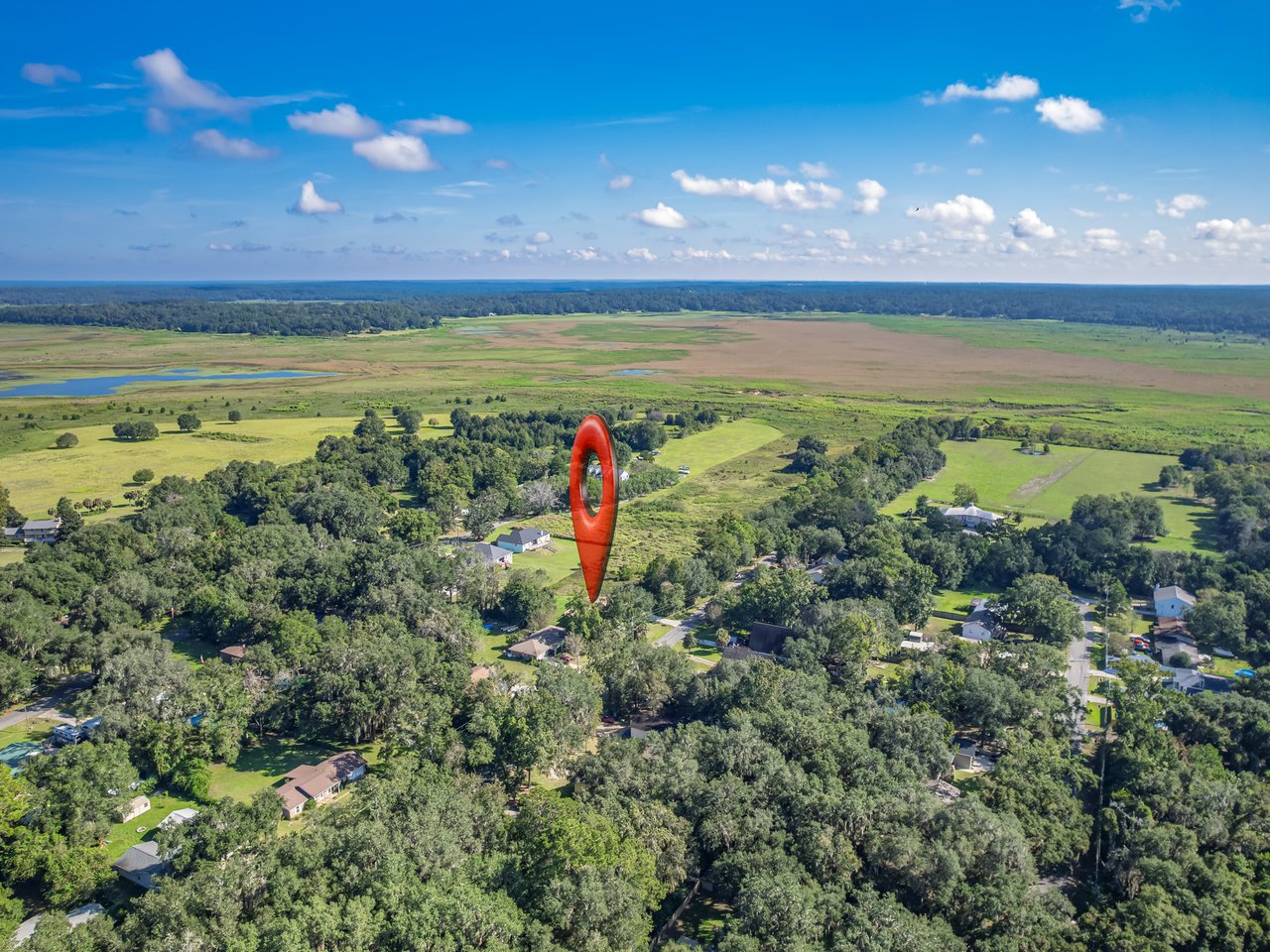Aerial view of wooded homes beside open wetlands, with a red map pin marking the property.