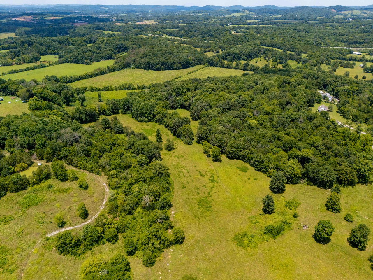 Aerial view of open meadows and wooded acreage with distant rolling hills.