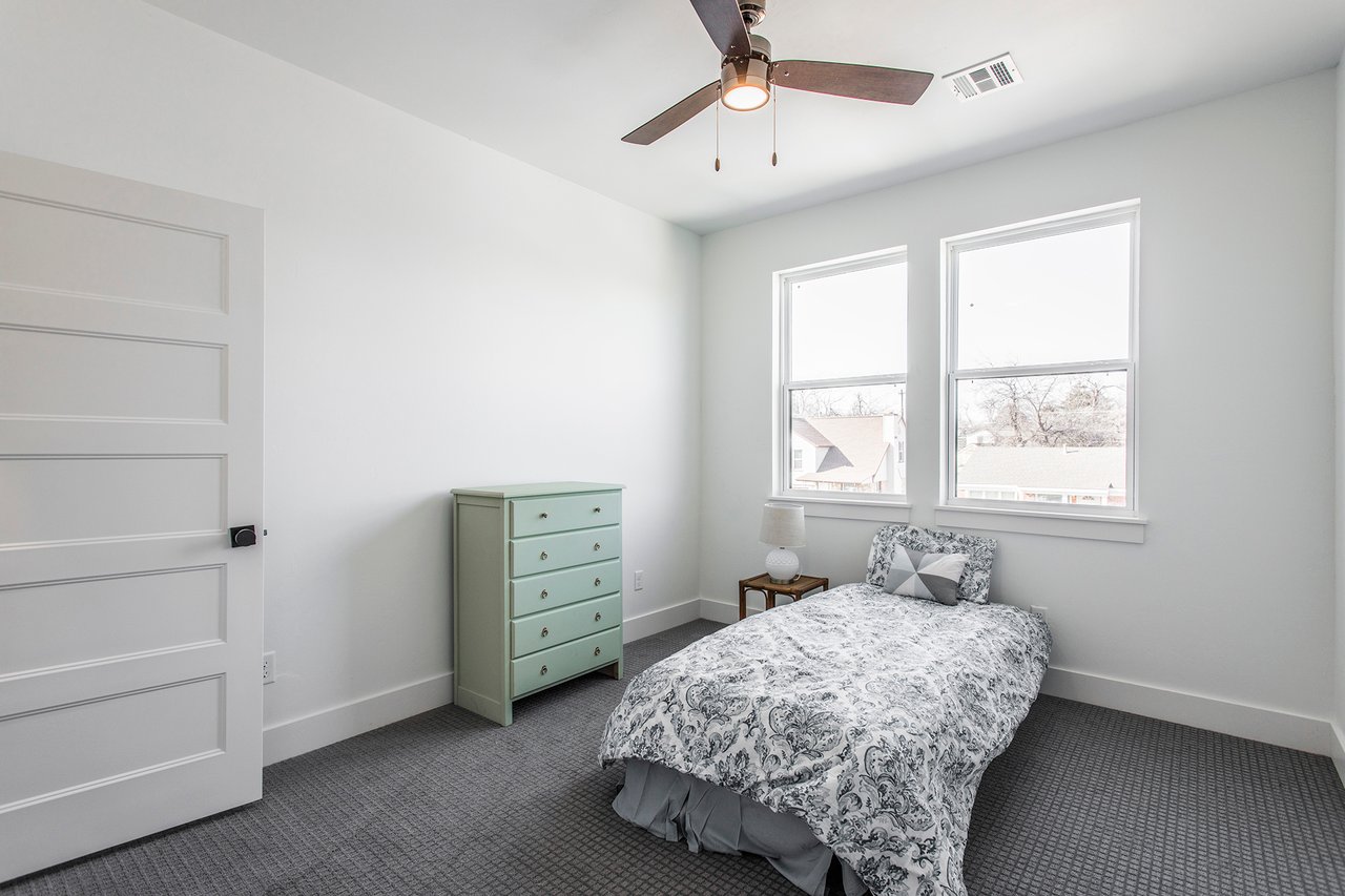 Bedroom with a patterned bed, pale green chest of drawers, and two bright windows.