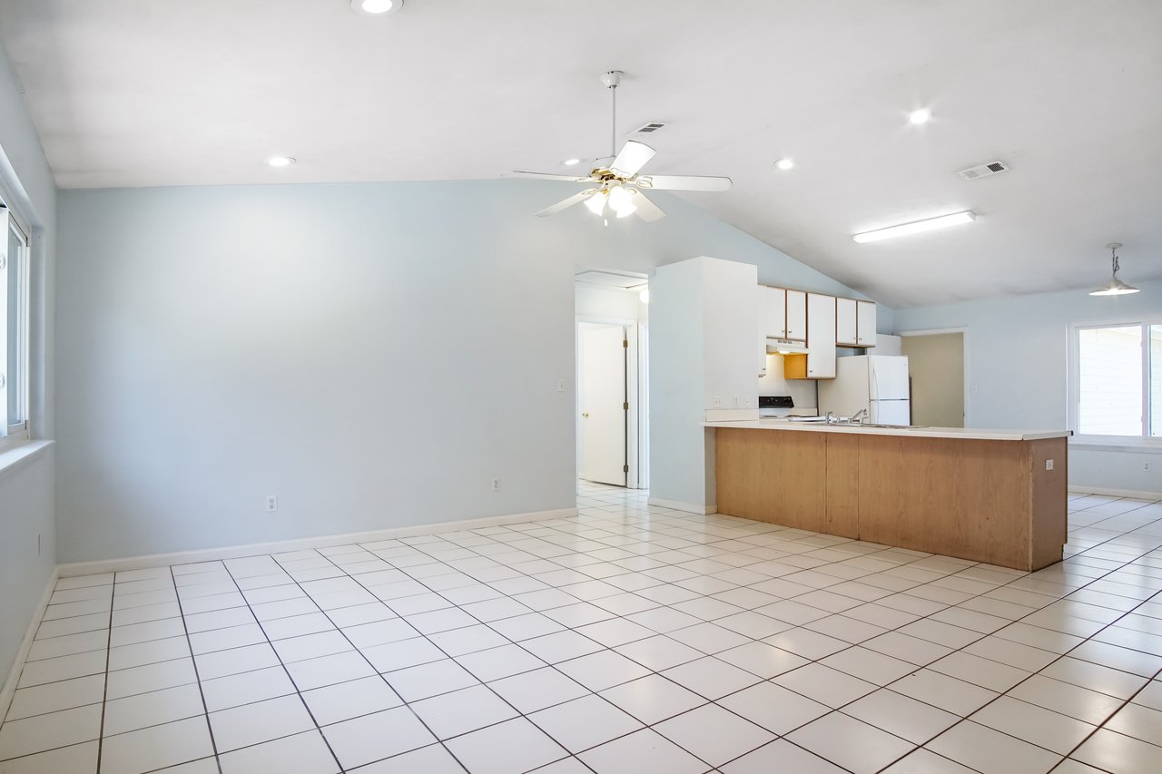 Spacious kitchen and dining area with light blue walls and white tiled floor. Wooden island, white cabinets, refrigerator, and ceiling fans create a bright, airy feel.