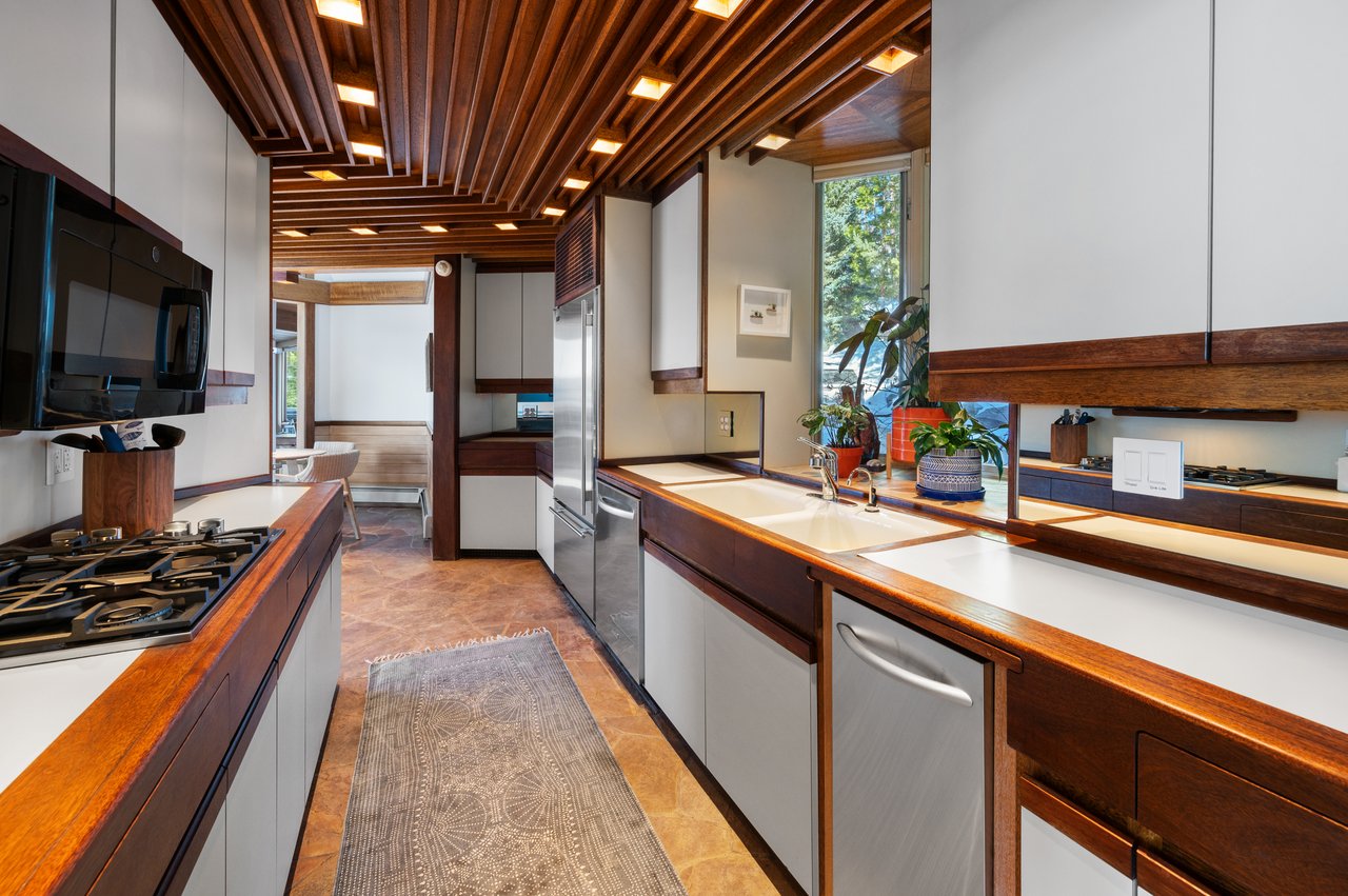 Galley kitchen with a slatted wood ceiling, white cabinets, stainless steel appliances, and a window-side sink.