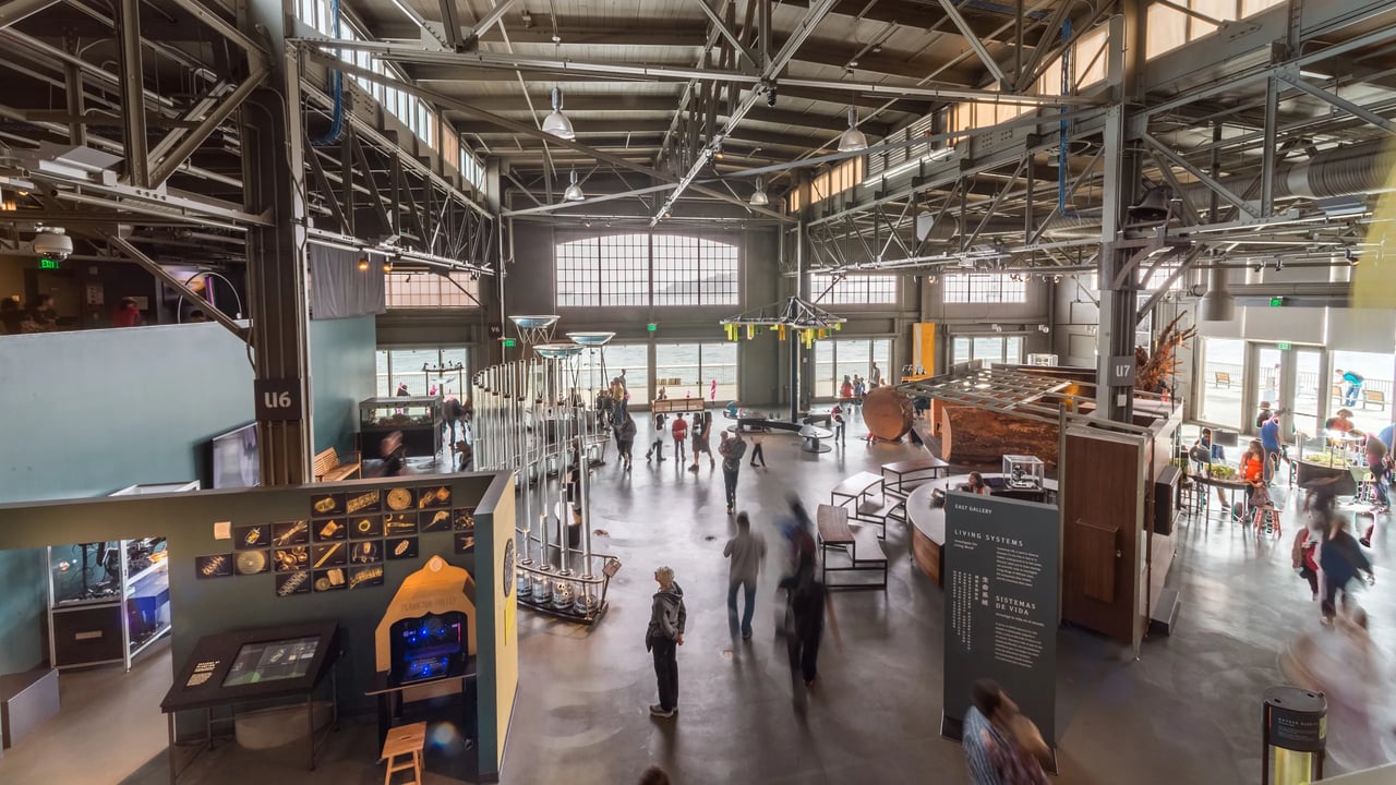 Visitors exploring interactive exhibit hall inside San Francisco museum with industrial ceiling