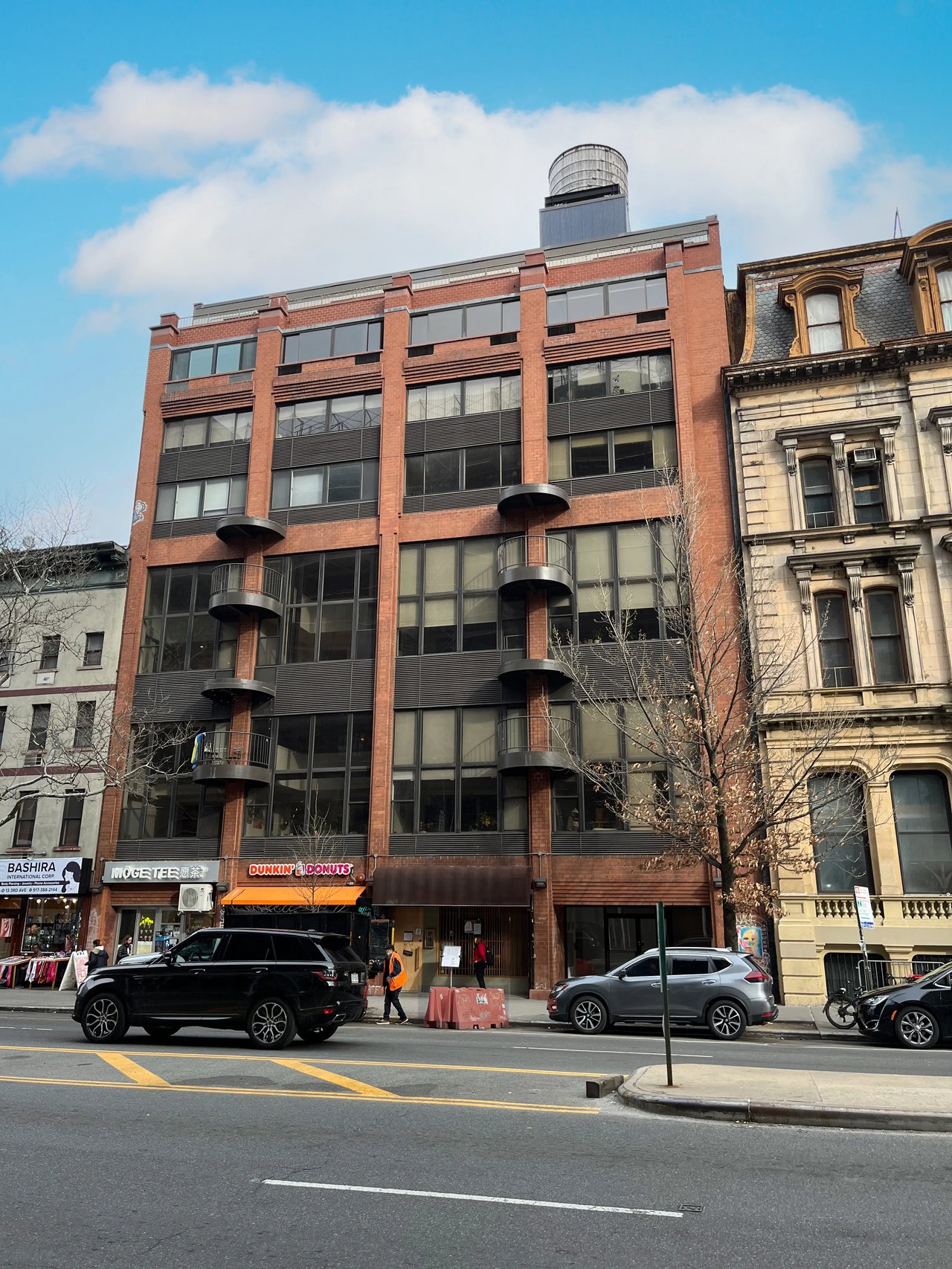 Red-brick mid-rise with curved balconies and a rooftop water tower above street-level shops.