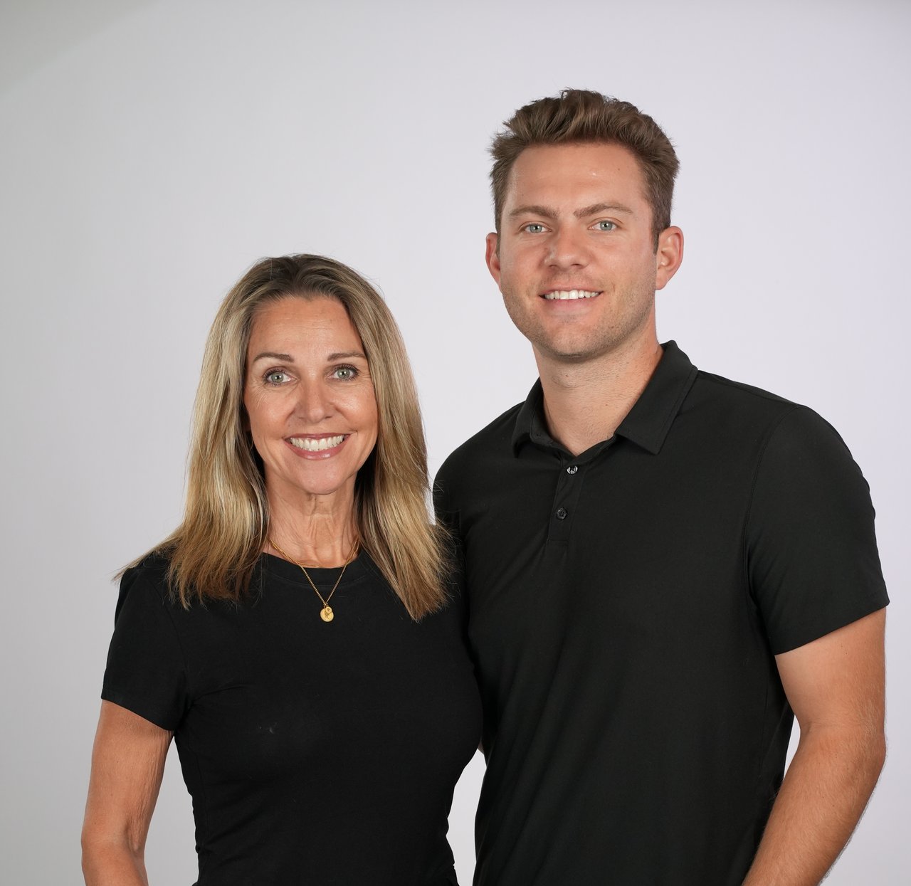 Two smiling adults pose together in black shirts against a light background.