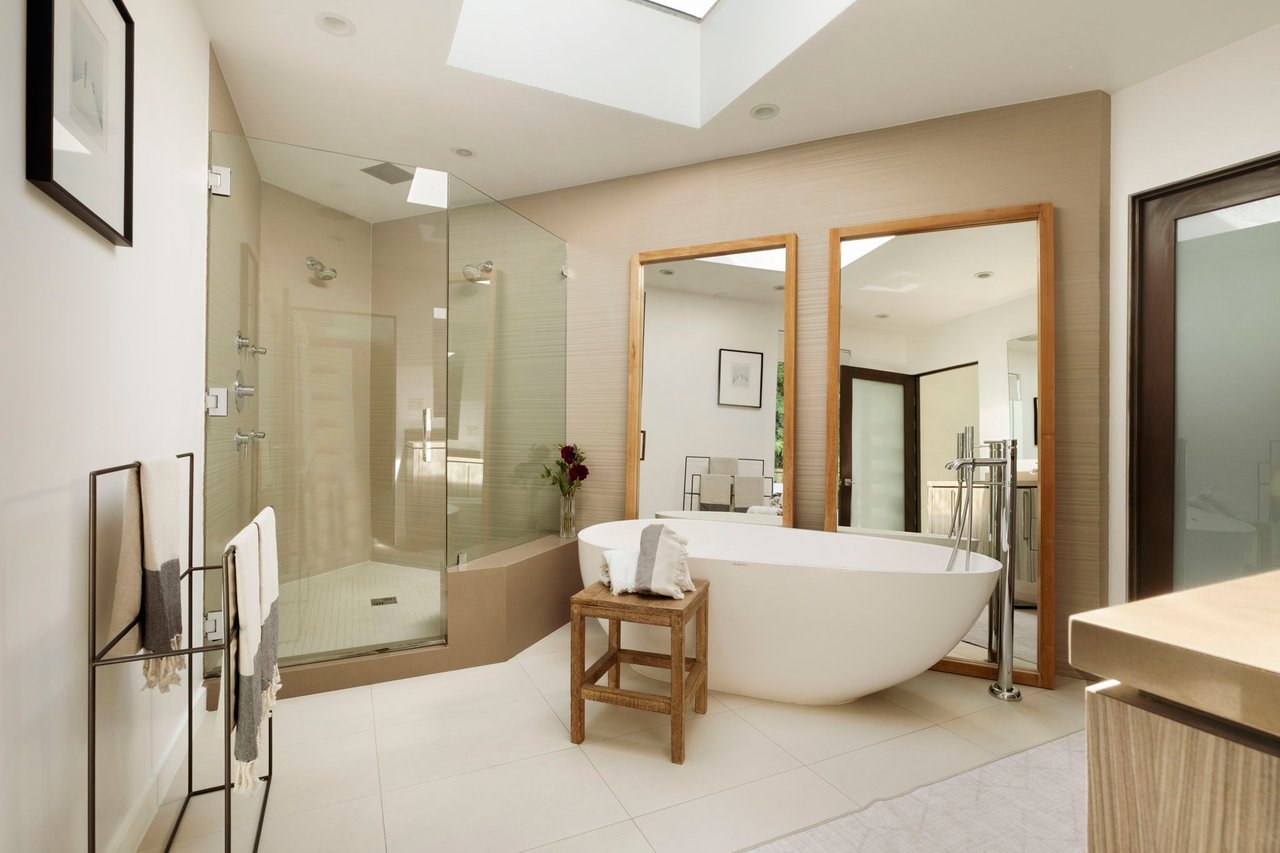 Modern bathroom with a freestanding soaking tub, glass shower, wood-framed mirrors, and skylight.