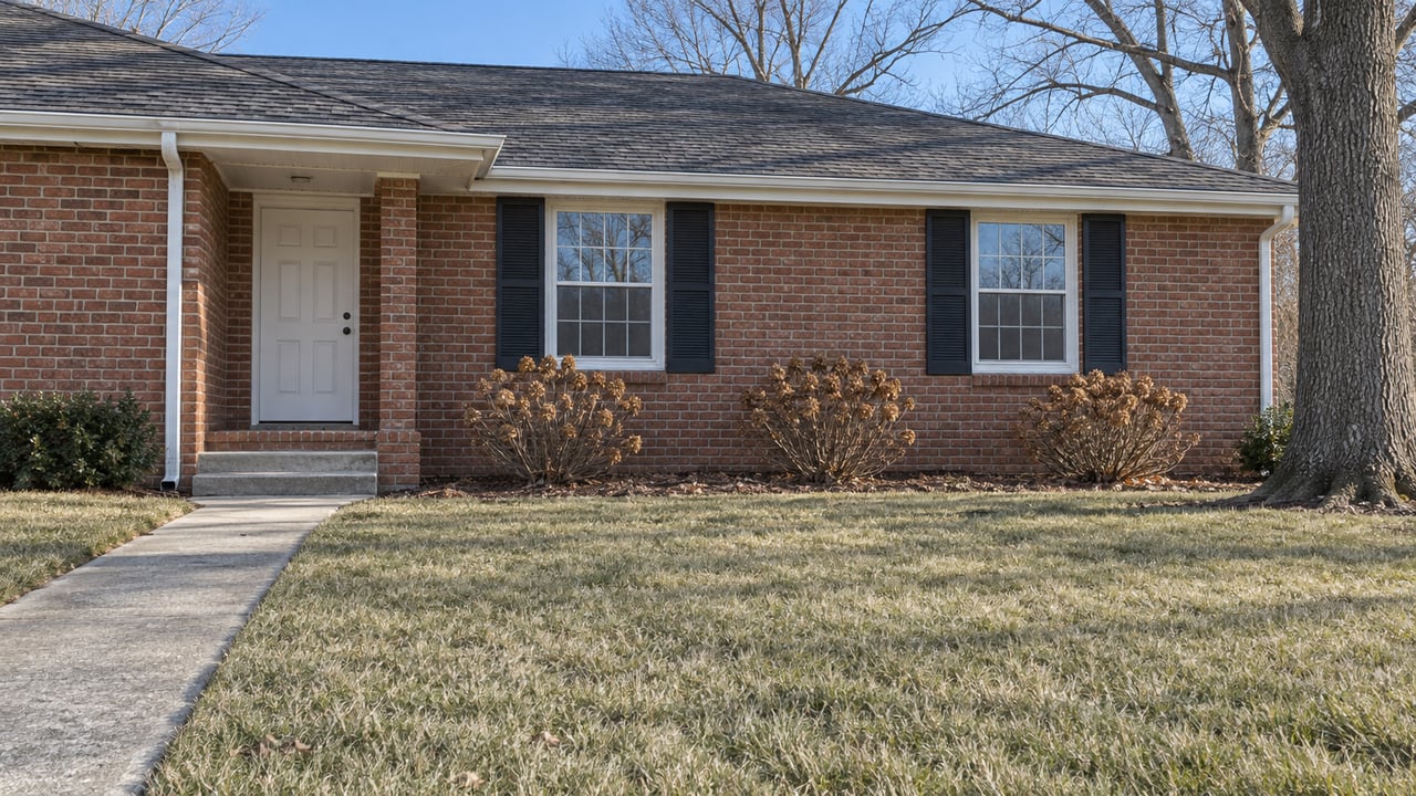 Winter sunlight on a red-brick ranch with white windows, a concrete front walk and a broad dormant lawn.