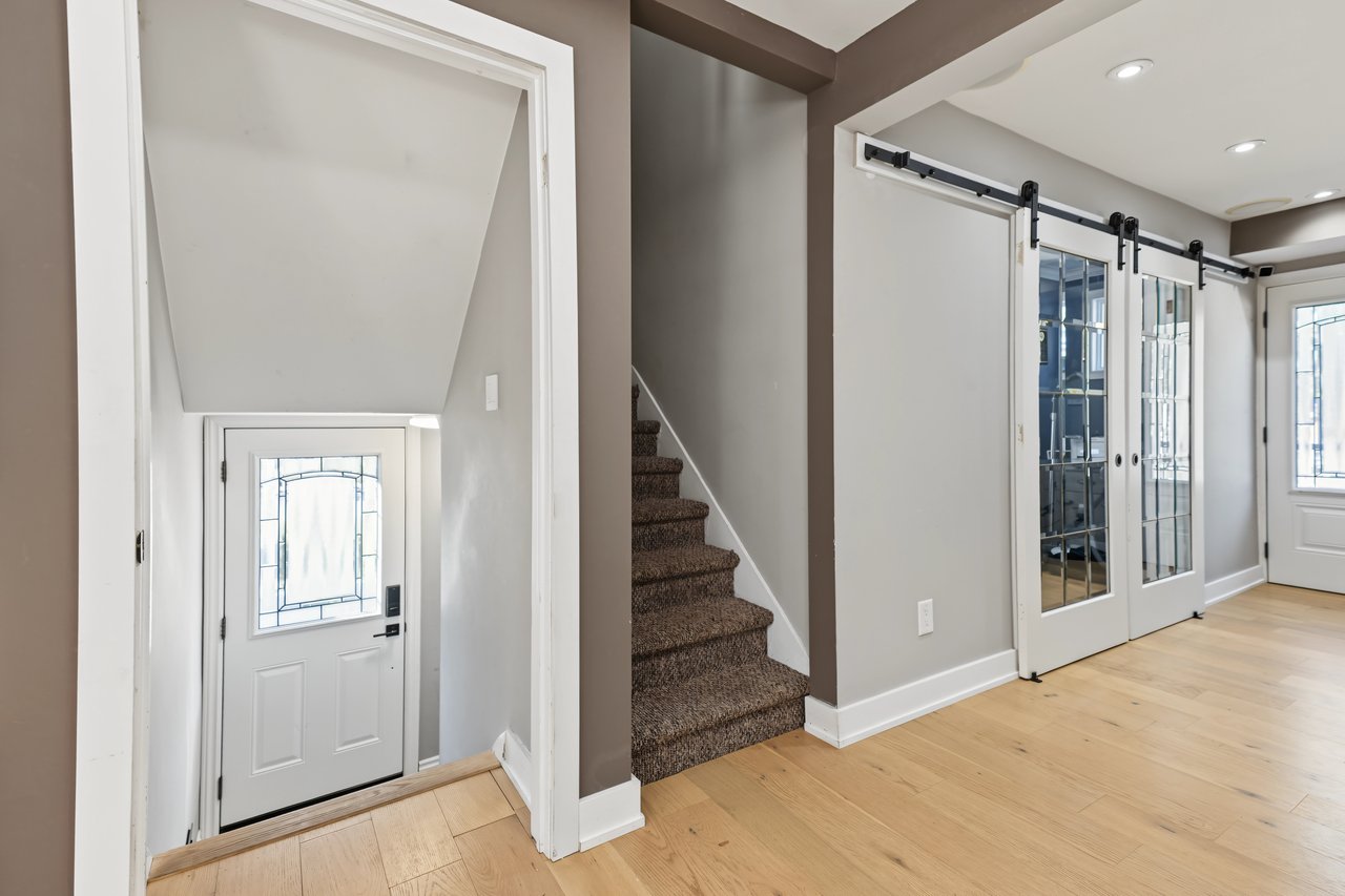 Entryway with a decorative-glass front door, carpeted stairs, and glass-panel sliding barn doors.