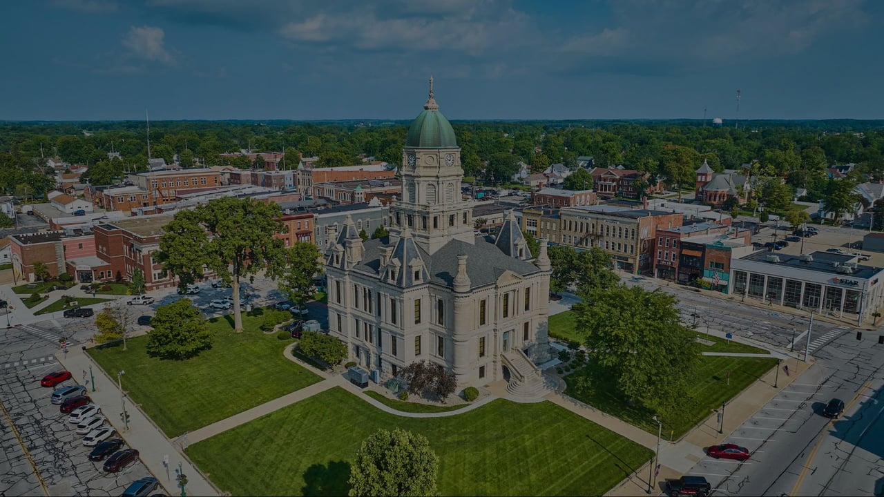 Aerial view of a town square centered on a historic courthouse with a clock tower.