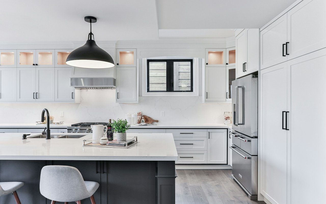 Modern white kitchen with a large island, stainless steel appliances, and a black pendant light.