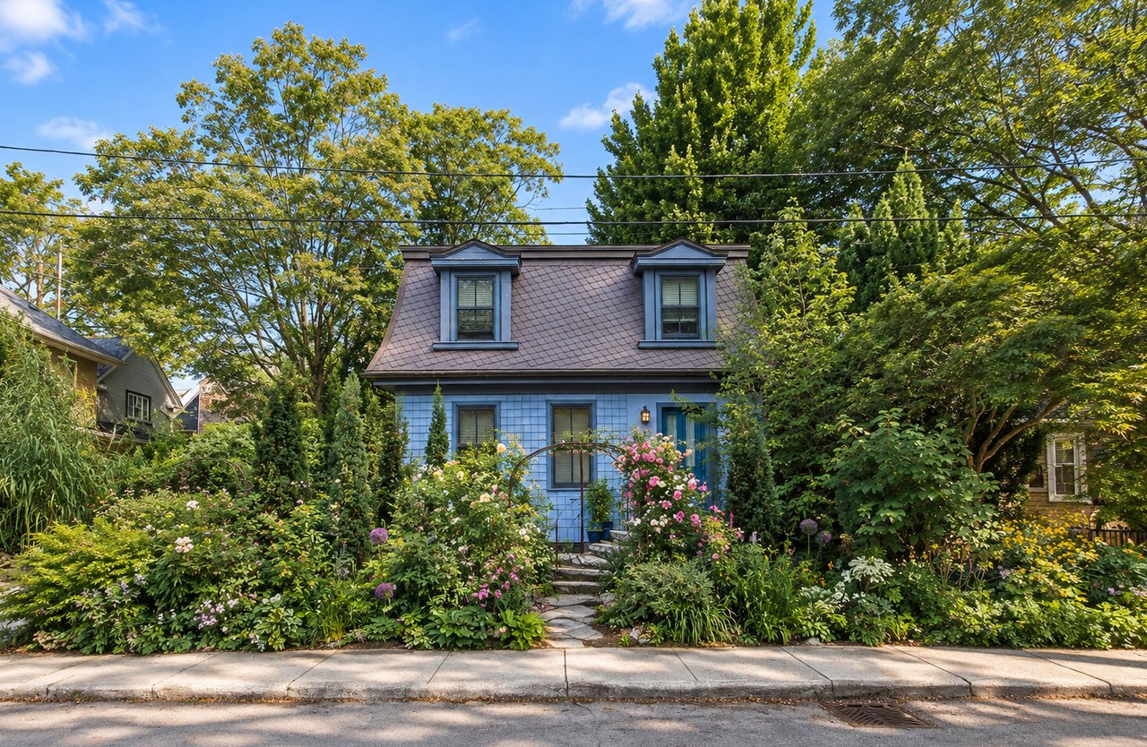 Blue house with dormer windows behind a lush, flower-filled front garden.