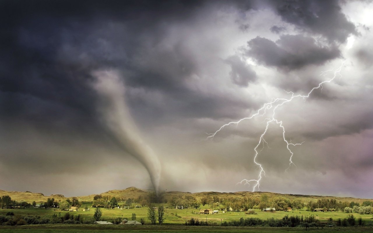 Tornado crossing a rural landscape beneath storm clouds, with lightning in the sky.