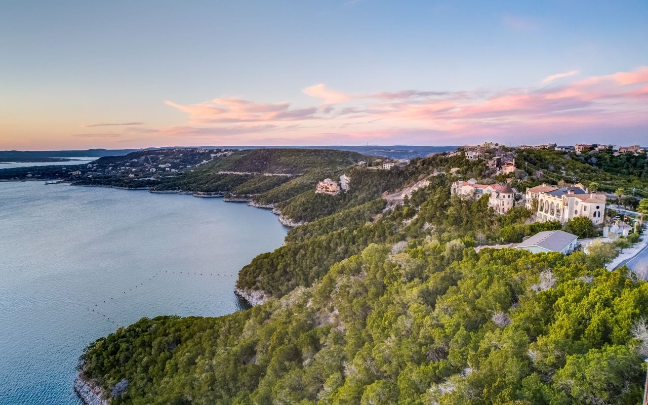 Aerial view of hillside homes along a wooded lake shoreline at sunset.