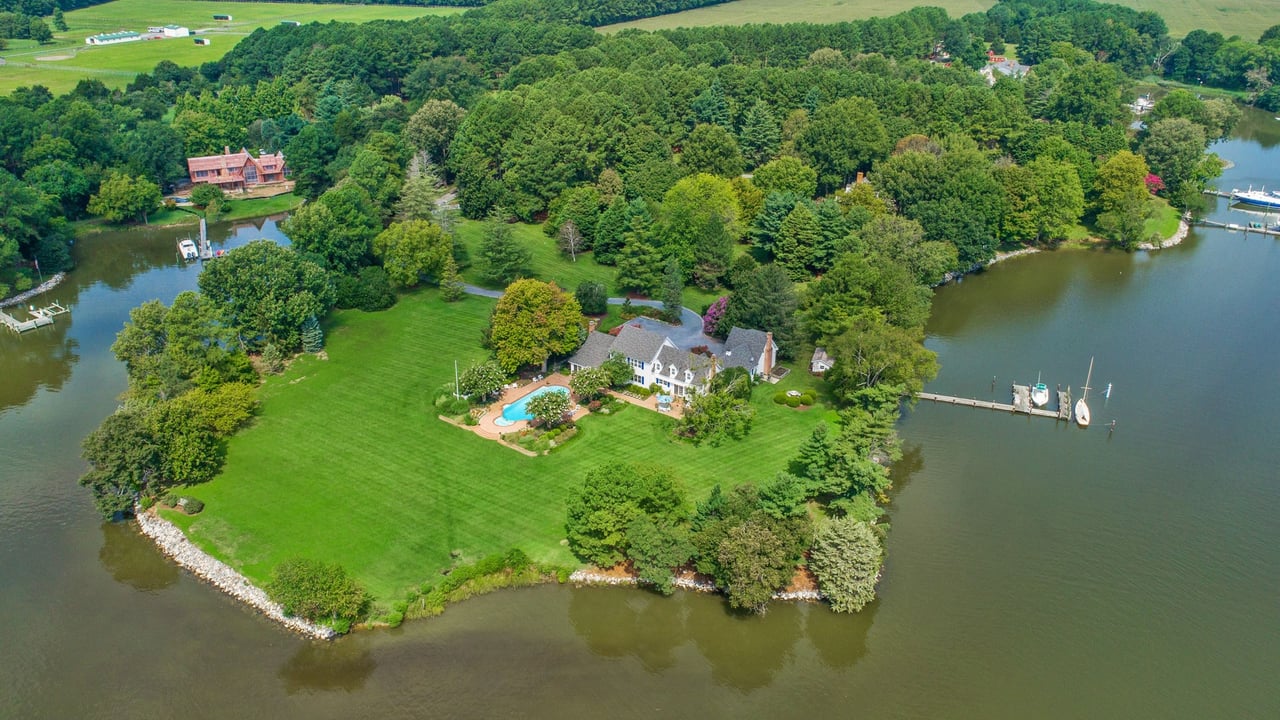 Waterfront home with a swimming pool, expansive lawn, and private dock, viewed from above.